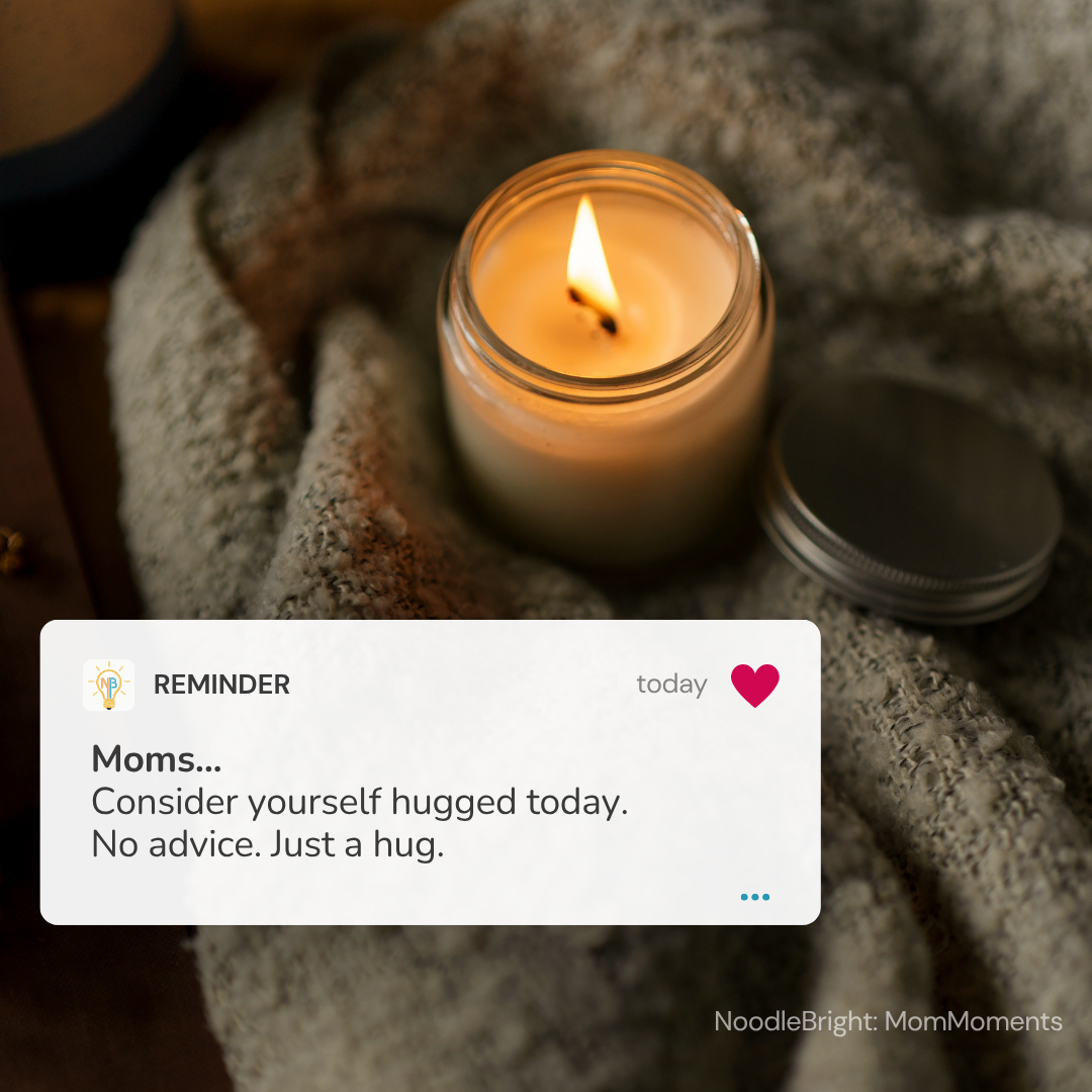 A lit candle in a clear glass jar sits on a soft gray knit blanket with its metal lid beside it. A white reminder card appears in the foreground with the text, 'Moms.