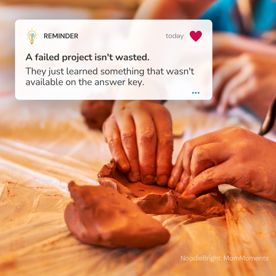 A close-up photo of a person's hands molding clay on a work surface, with a white reminder card overlaid at the top containing motivational text. The watermark 'NoodleBright: MomMoments' appears in the bottom right corner.