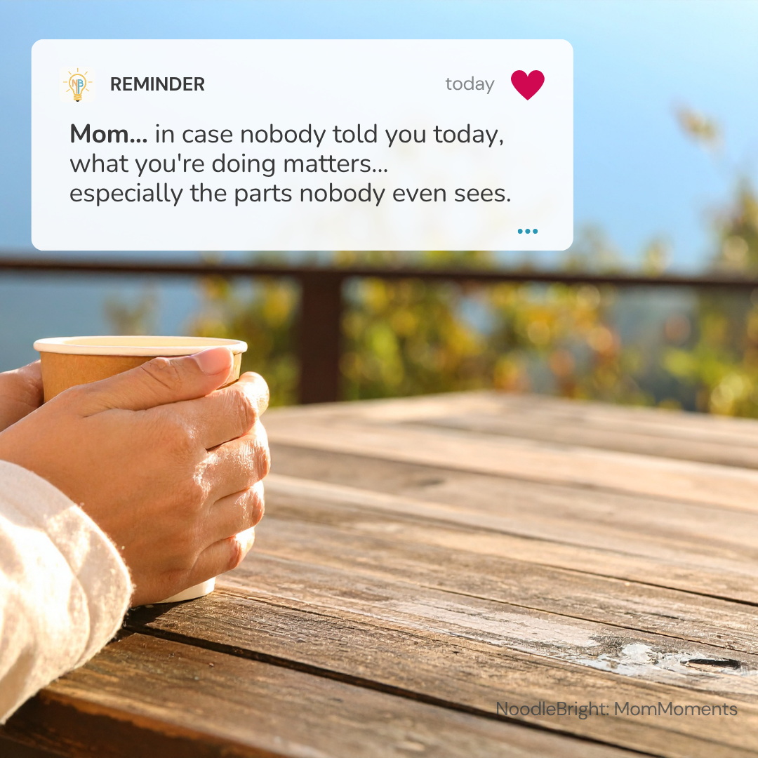 A mother holds a paper coffee cup on a wooden table outdoors, with a soft-focus background of water and sky. A white reminder card at the top reads, 'Mom.